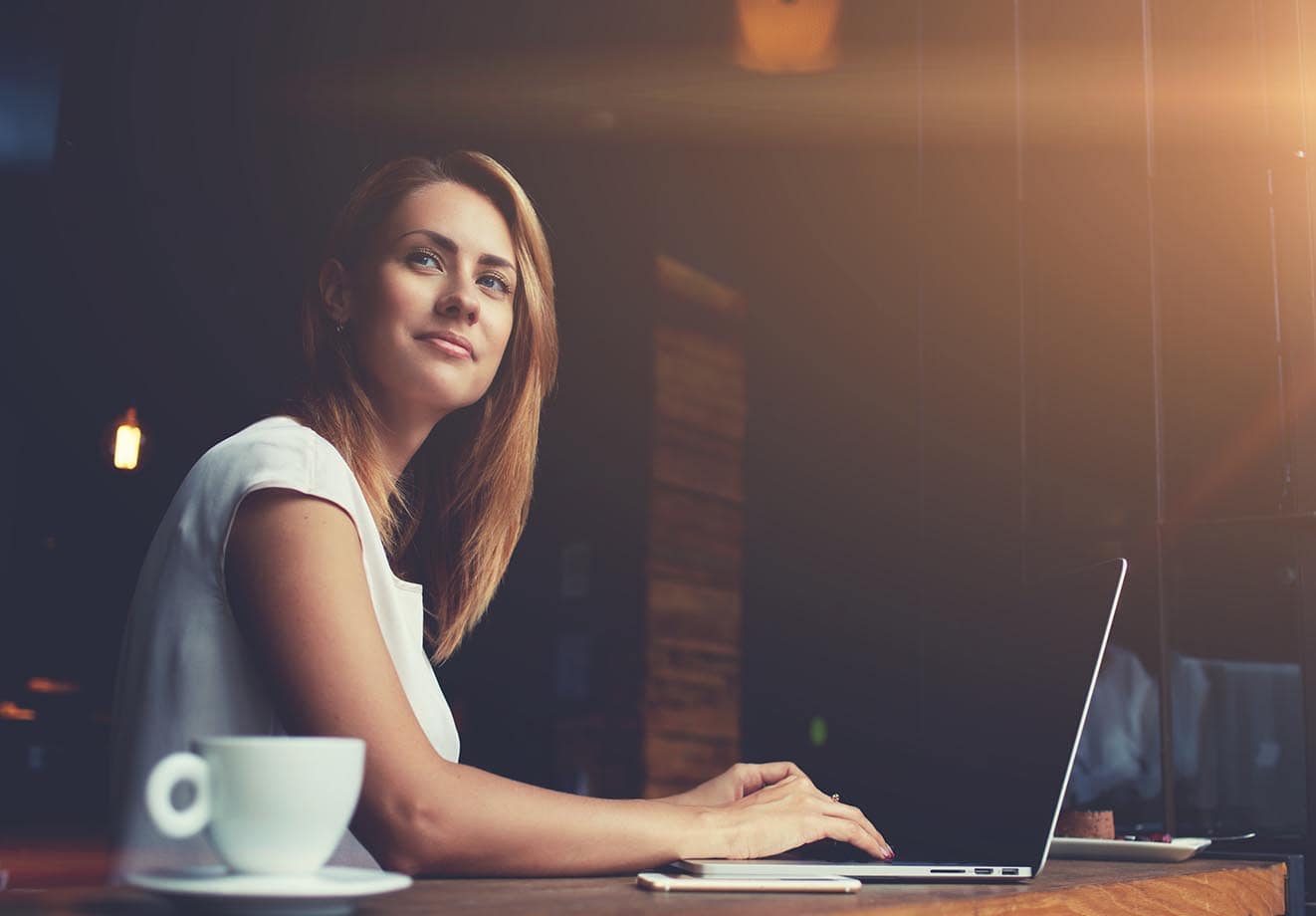 Woman working on her laptop with a contemplative expression on her face