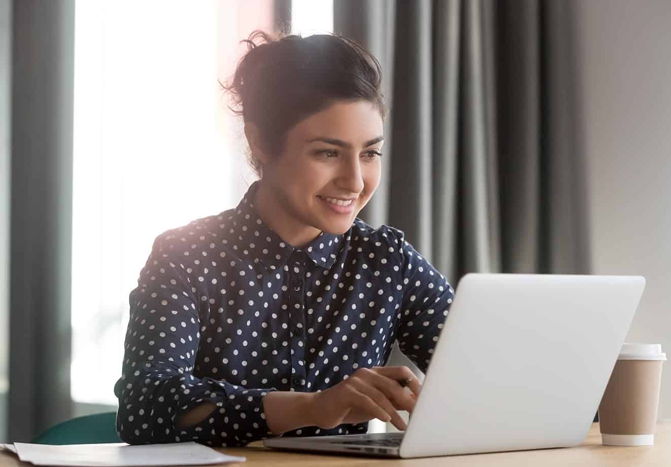 A person sits at a desk on a laptop with a cup of coffee next to them