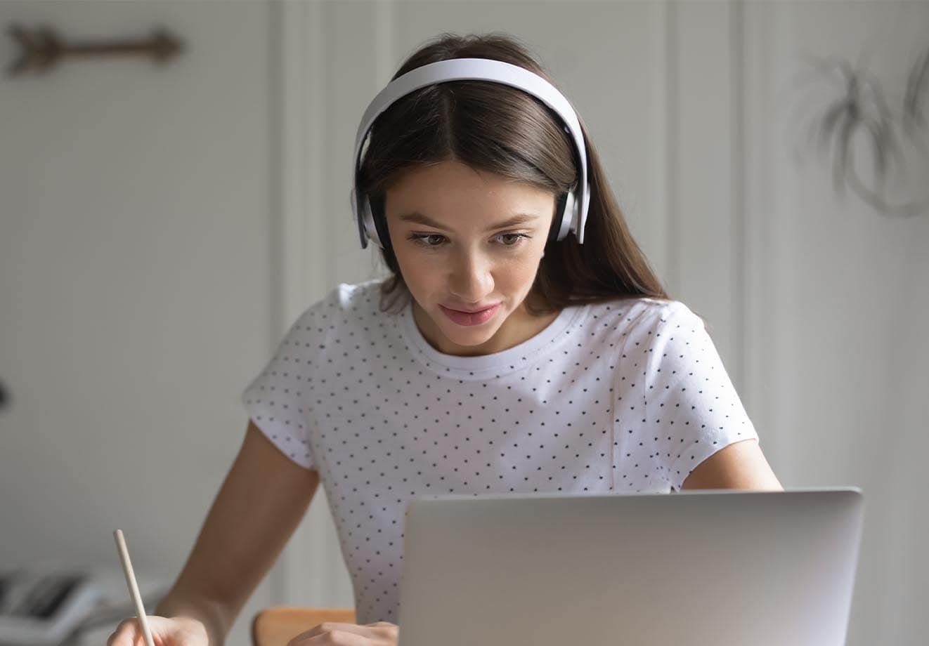 A young girl with headphones takes notes off her laptop