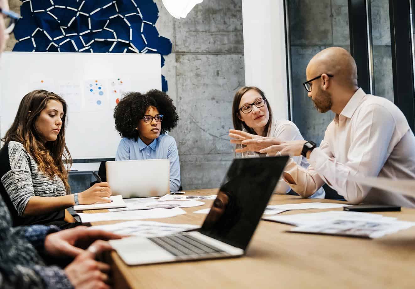 four higher education learning designers sit at a table with their laptops and notes, discussing the biggest challenges they've faced this year
