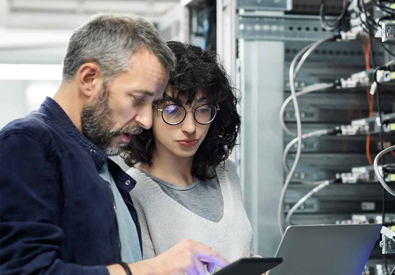 Man and woman standing in front of a panel with wires looking at tablet screens