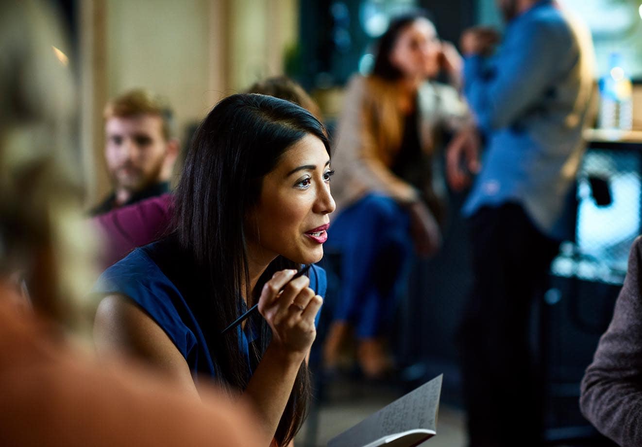 A woman discusses an idea with a notepad in her hand in the midst of her colleagues