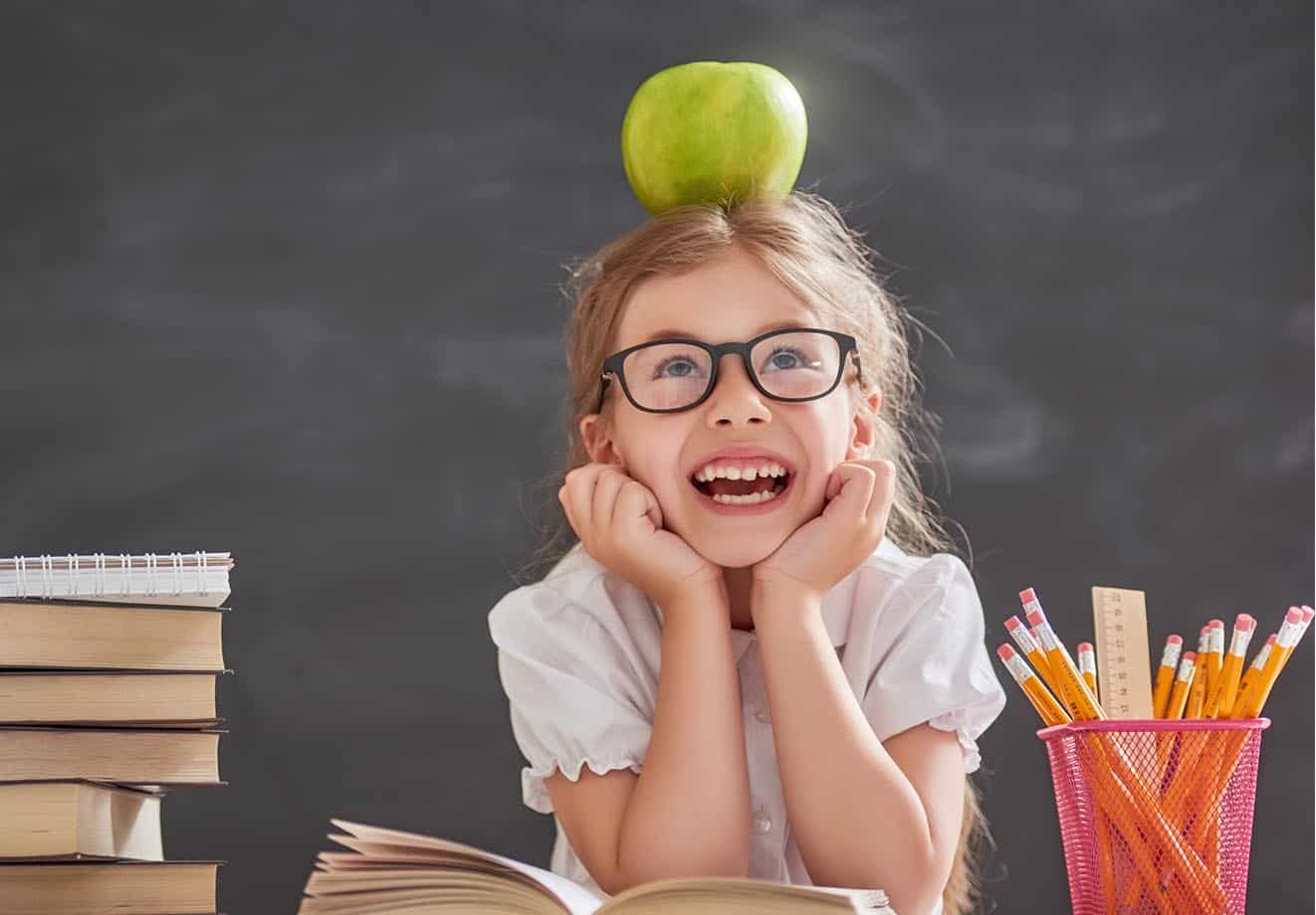 student smiling and balancing a green apple on her head