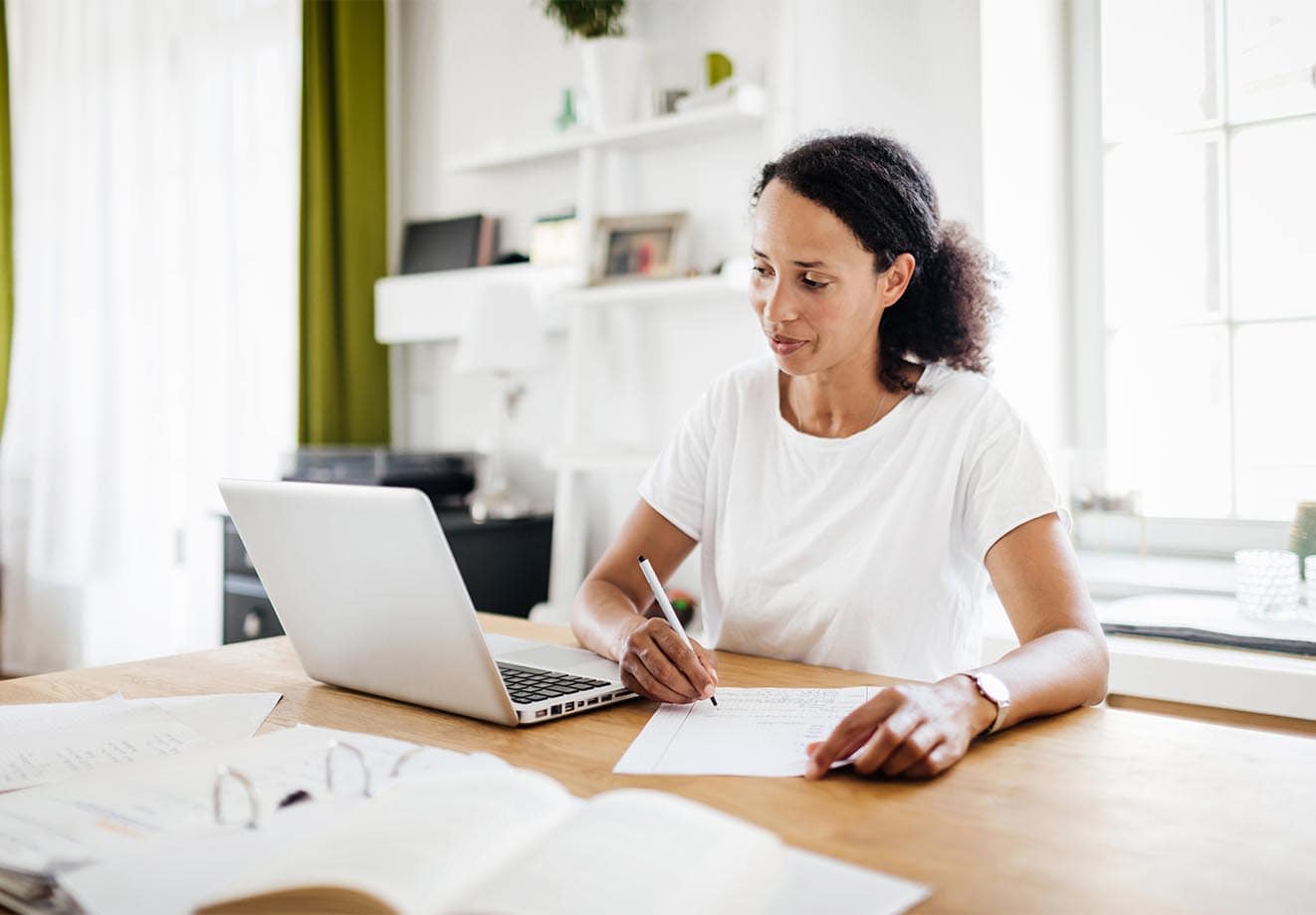 A person looks at a laptop and writes on a page as they figure out their return on investment