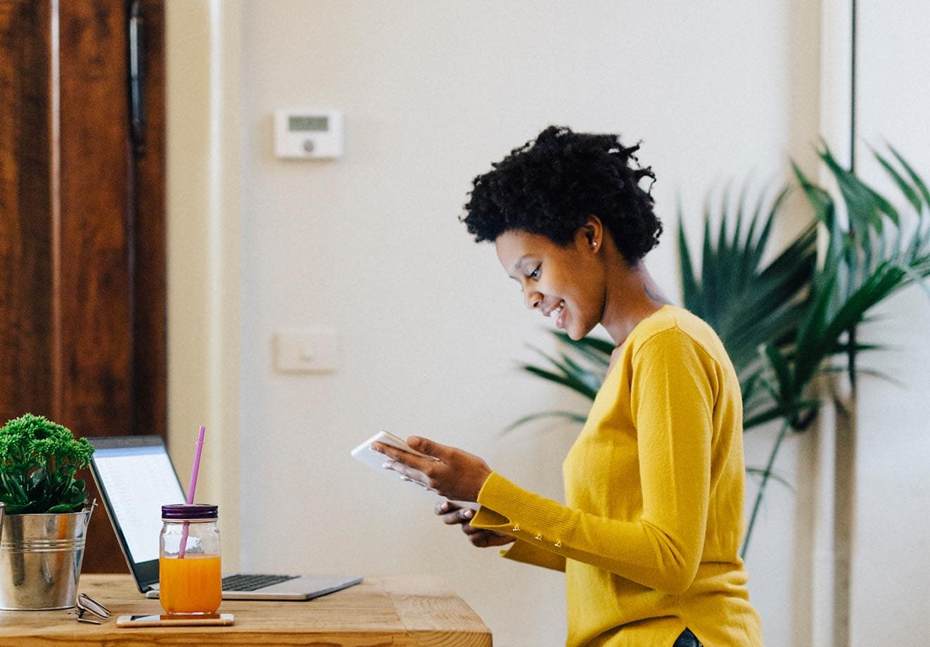 woman wearing a yellow sweater and looking down at a tablet in her hands