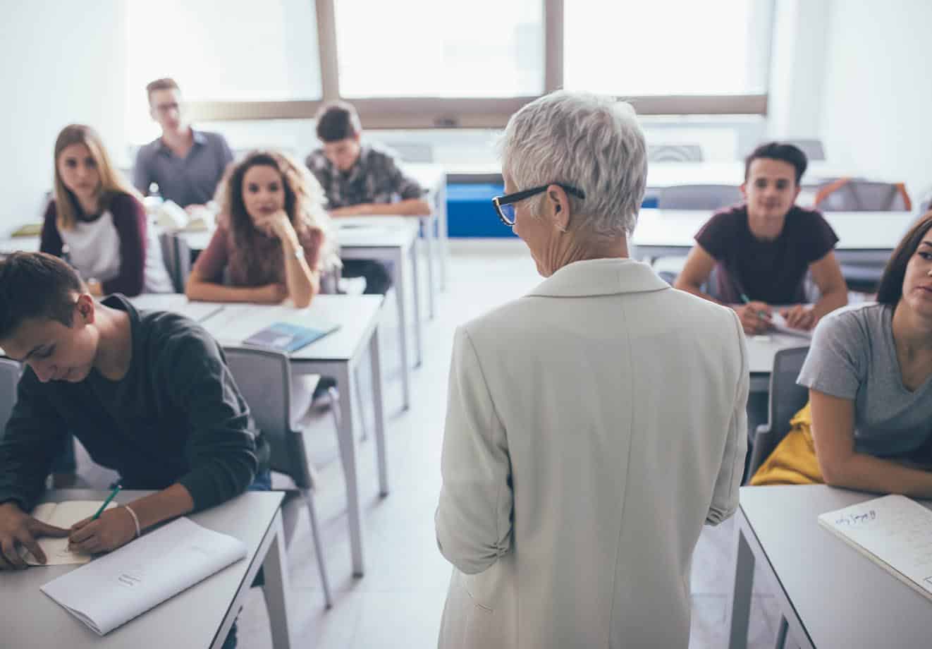 An instructors stands at the front of a class and interacts with students.