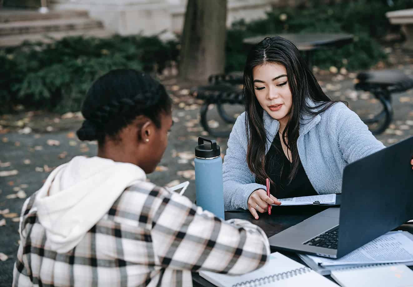 students sitting at table outside working on laptop
