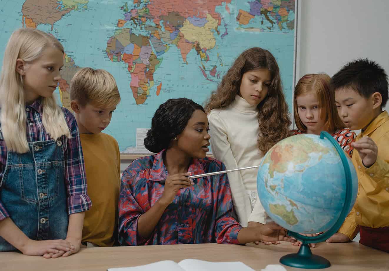 teacher pointing to globe with students beside her