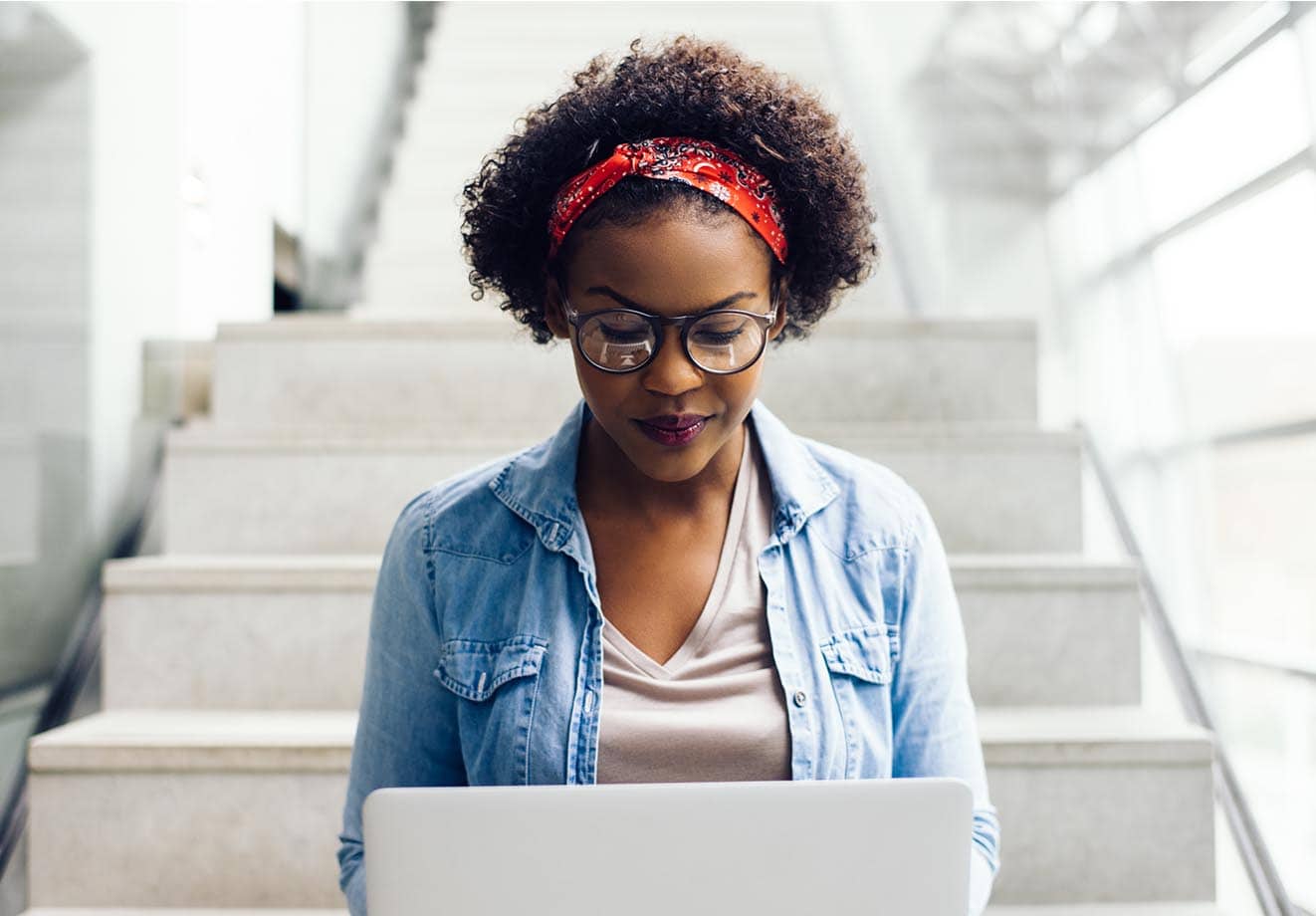 young black woman sitting on stairs working her laptop