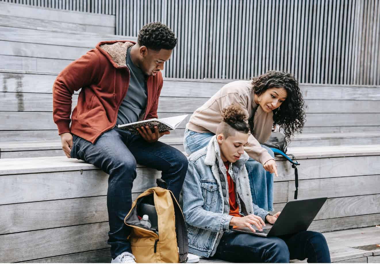 Group of 3 students looking at laptop outside