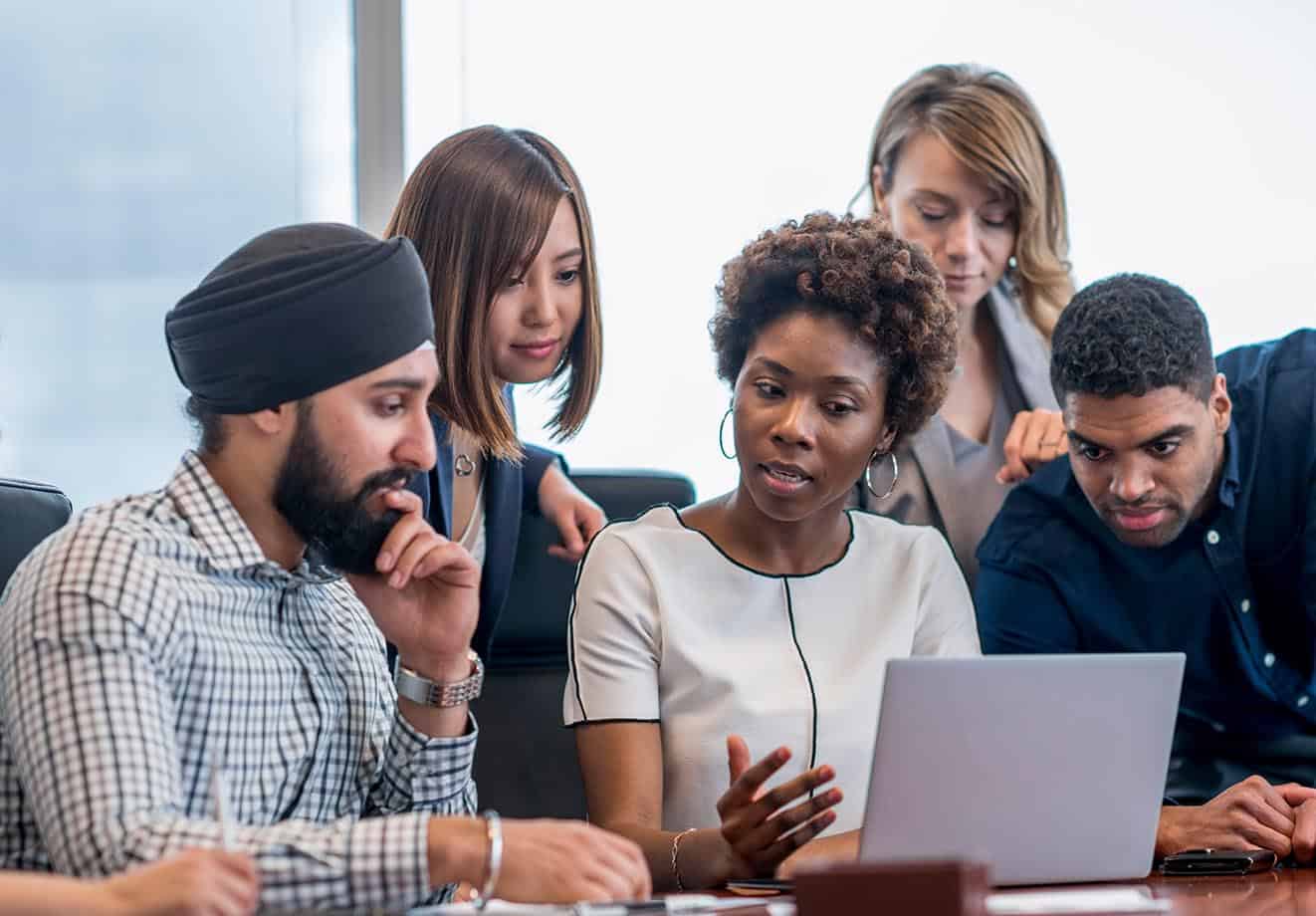 A group of employees crowd around a laptop sitting on a table.