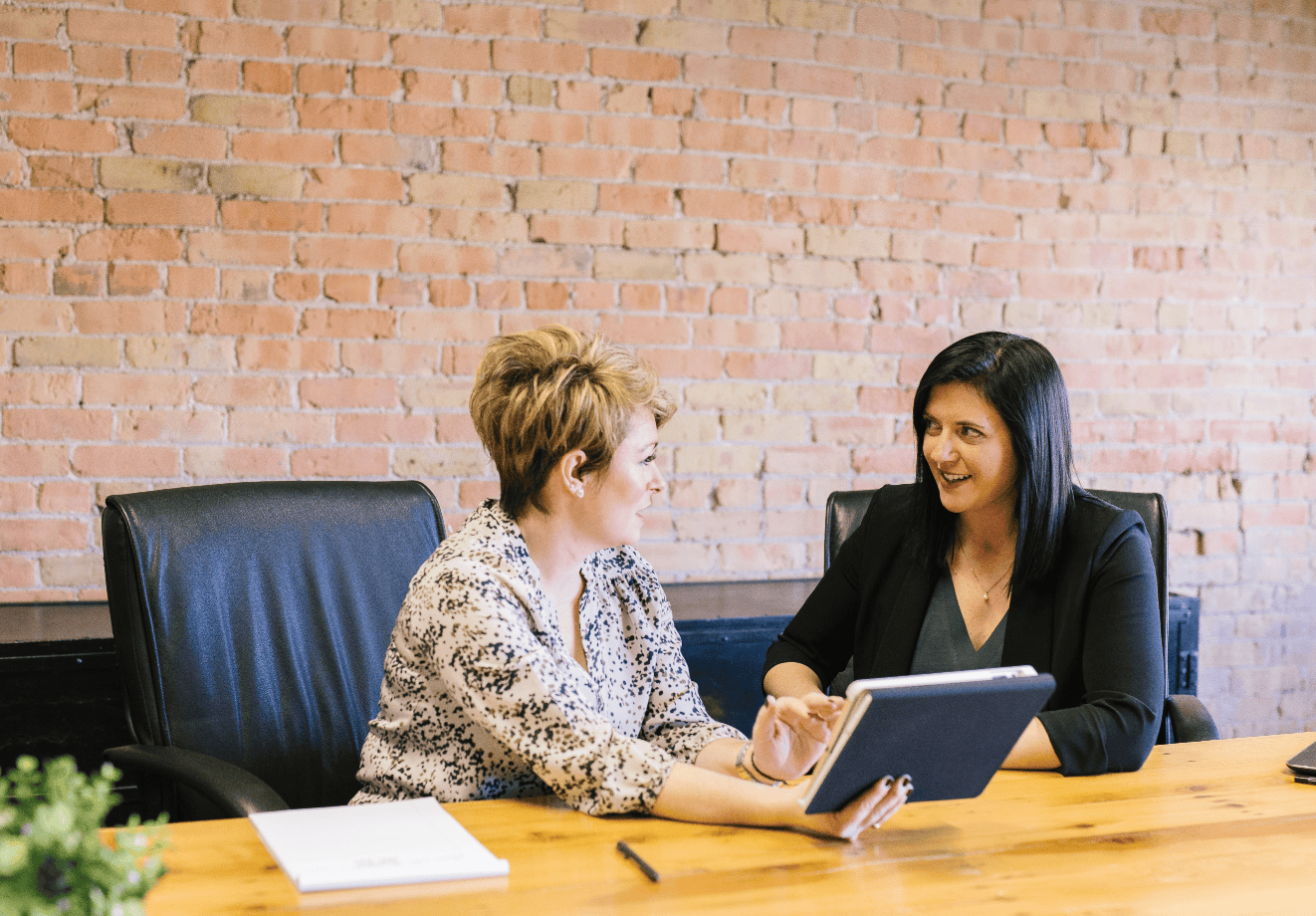 Two colleagues sit side by side at a desk consulting a tablet