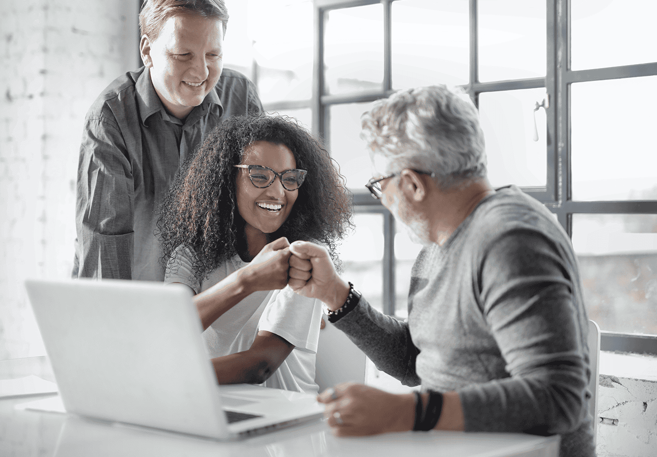 Three employees celebrate at a desk in front of a laptop.