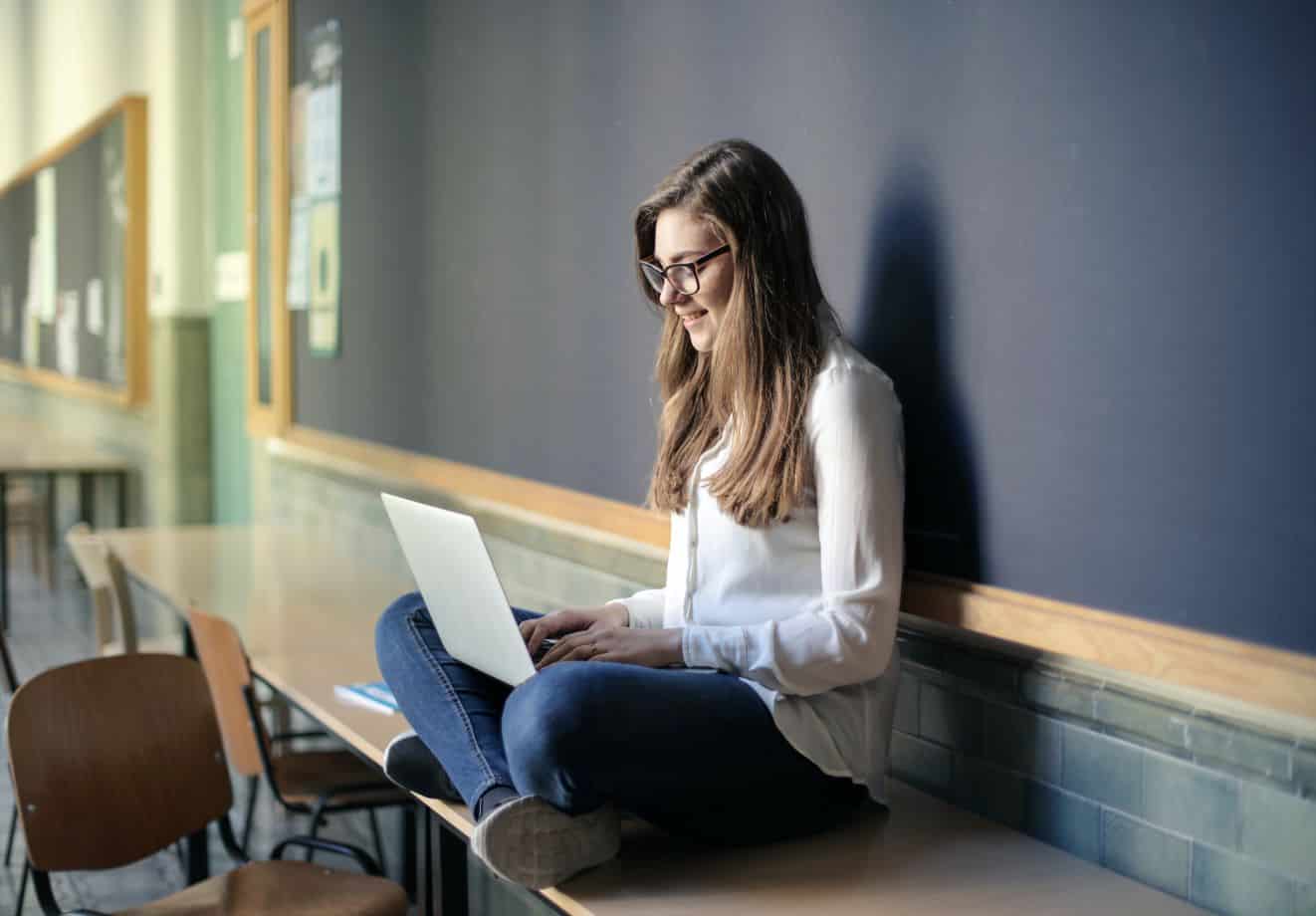 Girl sitting on desk and studying on laptop in classroom