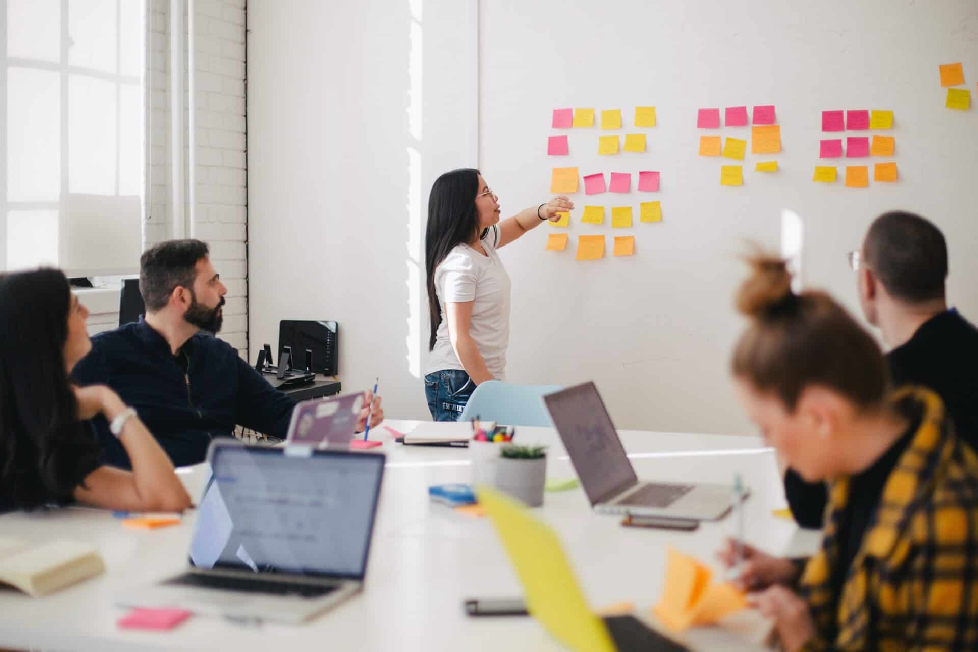 A group of teachers gather in a conference room for professional development; four are seated at laptops and one is at the whiteboard