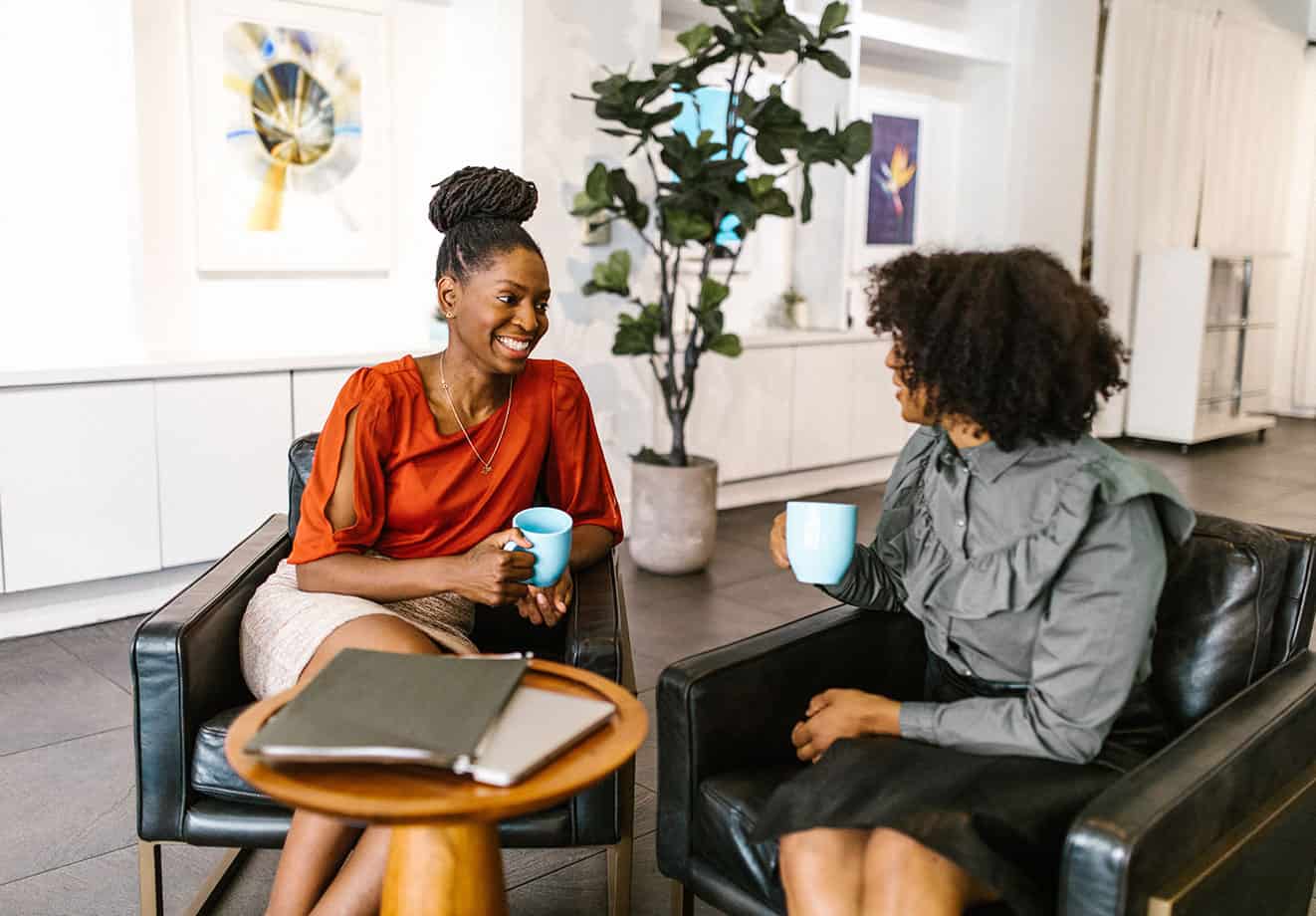 Two women sitting in chairs chatting while holding coffee mugs