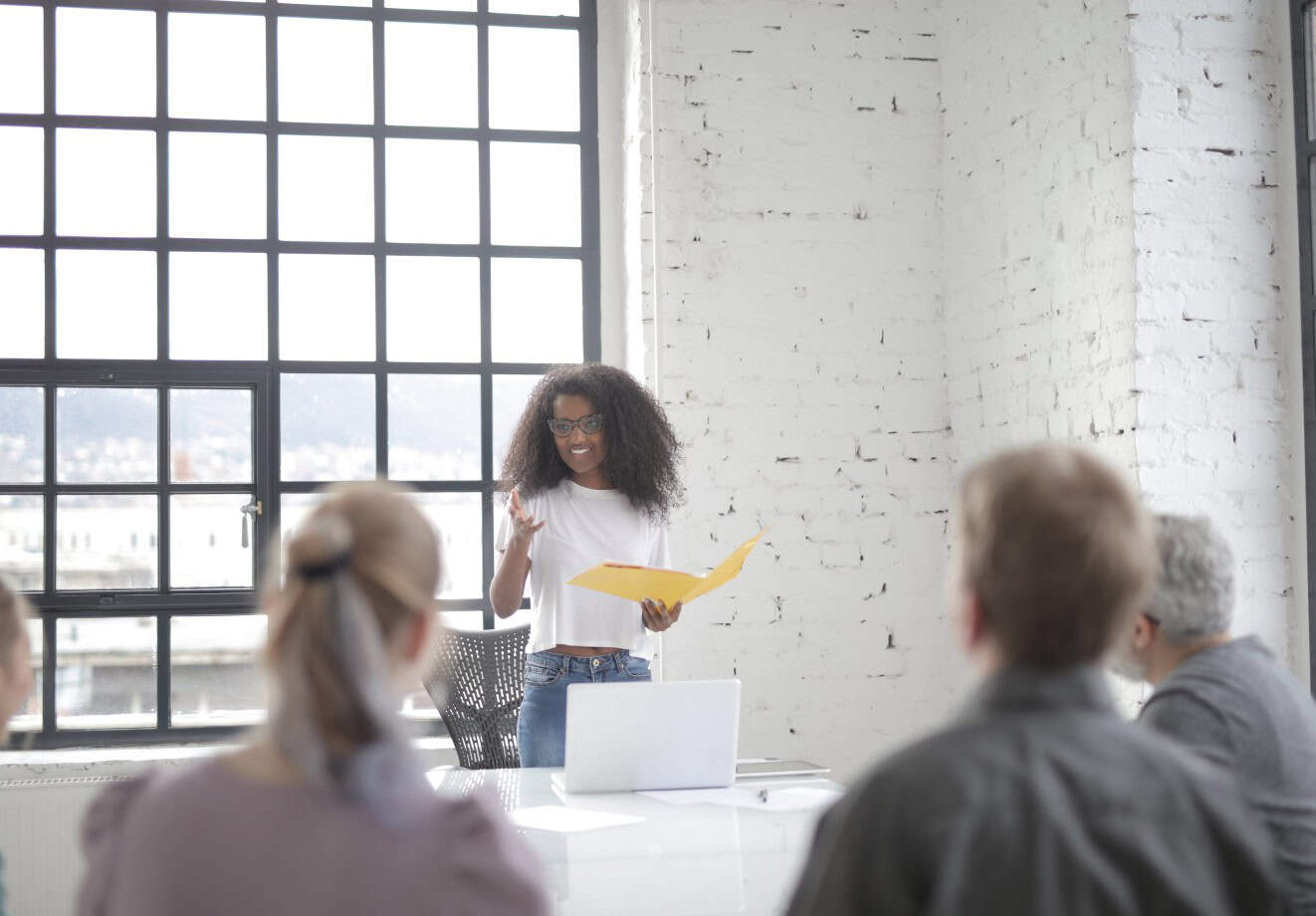A woman standing in a boardroom at the front of the table and talking to three colleagues