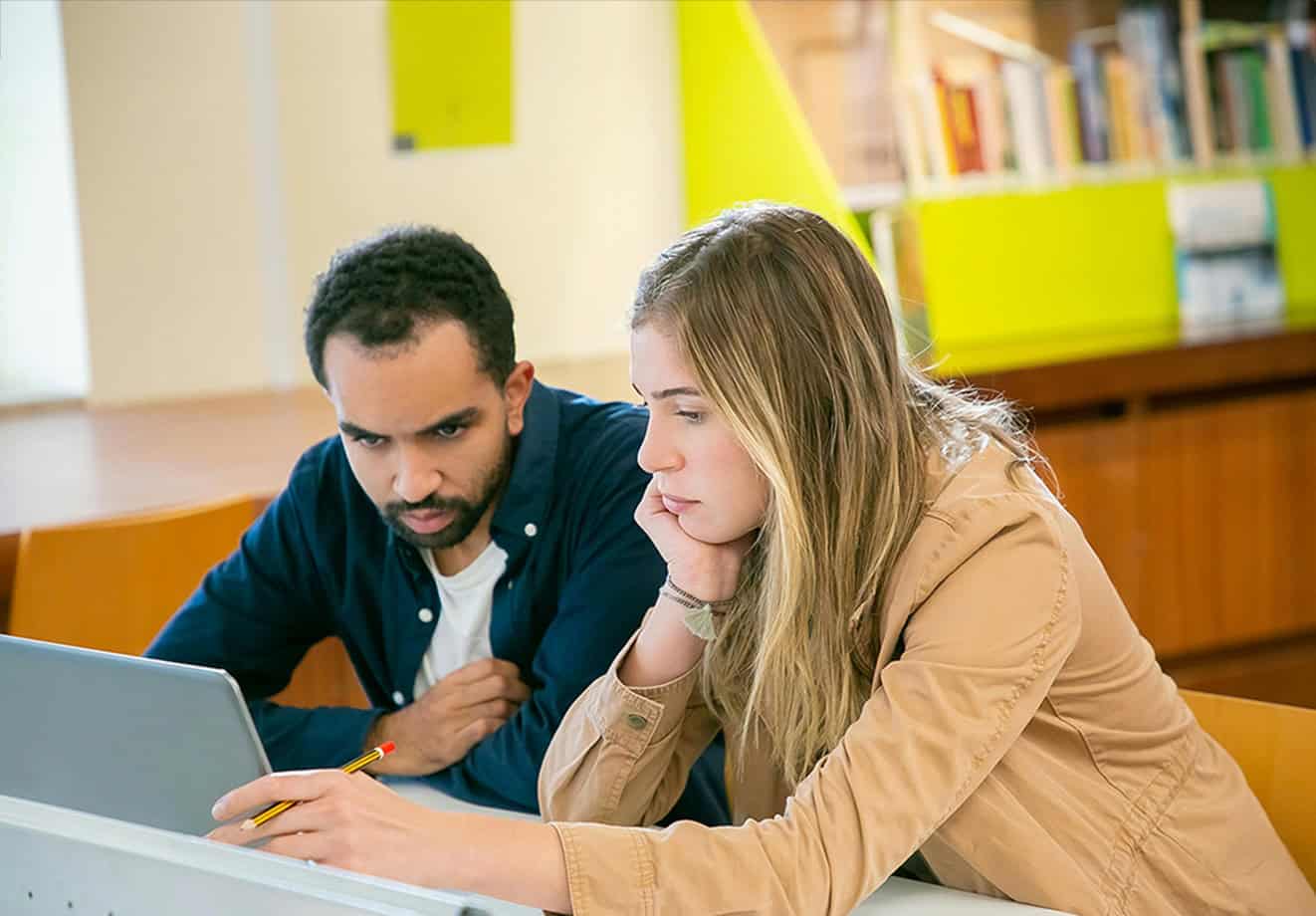 Two students working on laptop in library