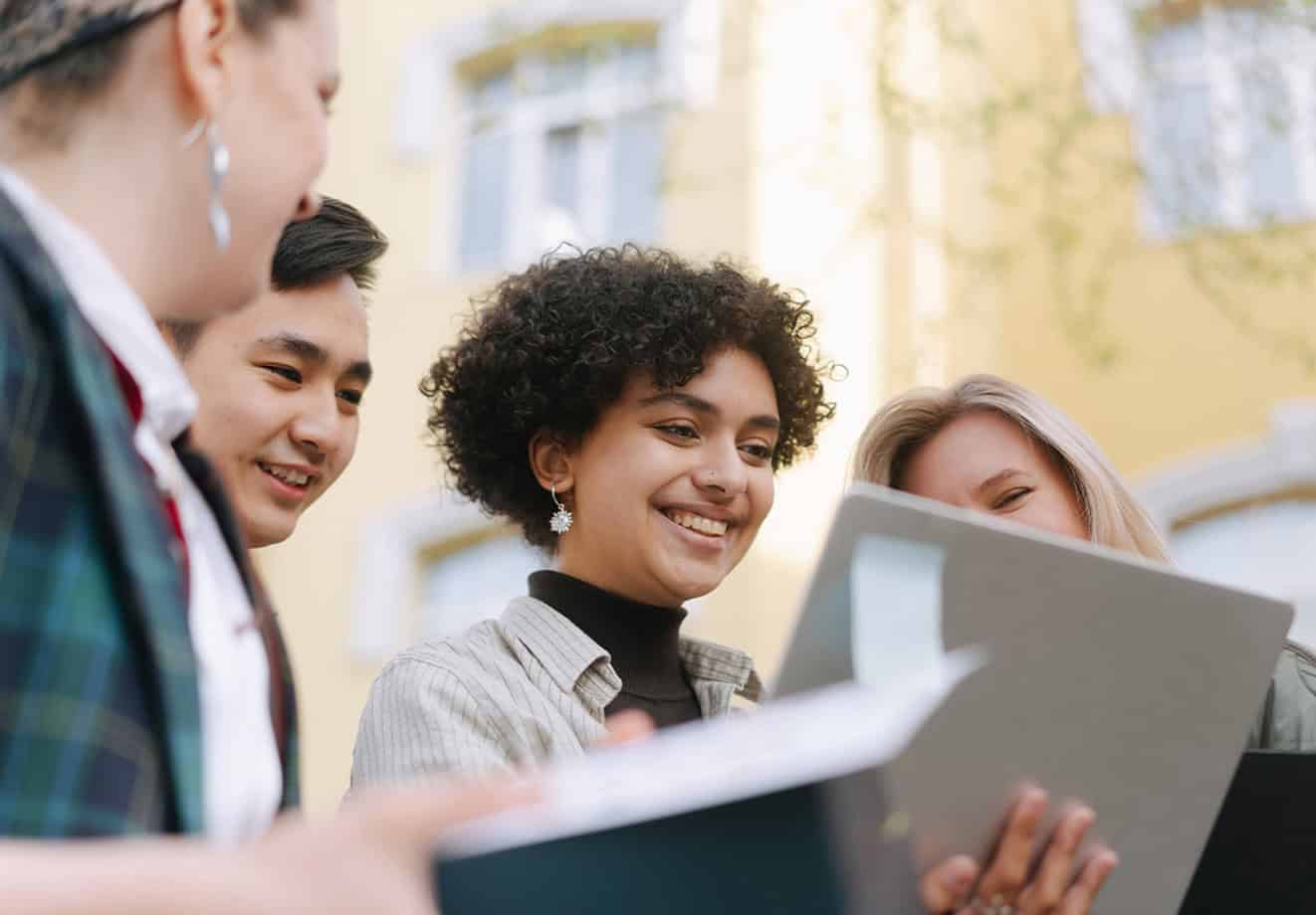 Four students gathered around laptop outside school