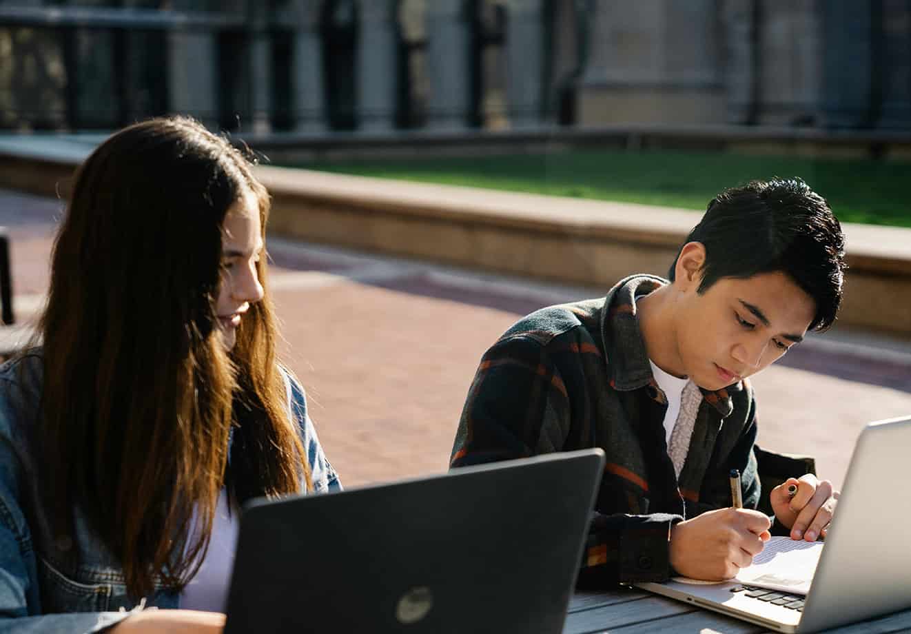 Two students working on laptops outside stone university