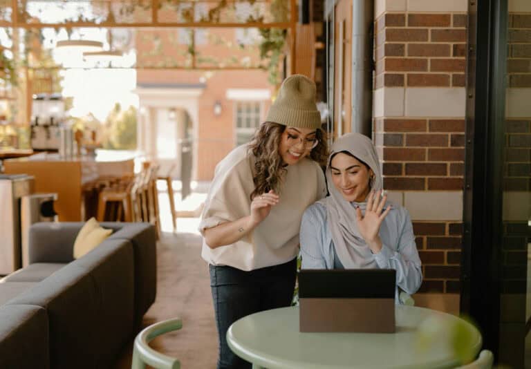 Two women waving to someone on a tablet