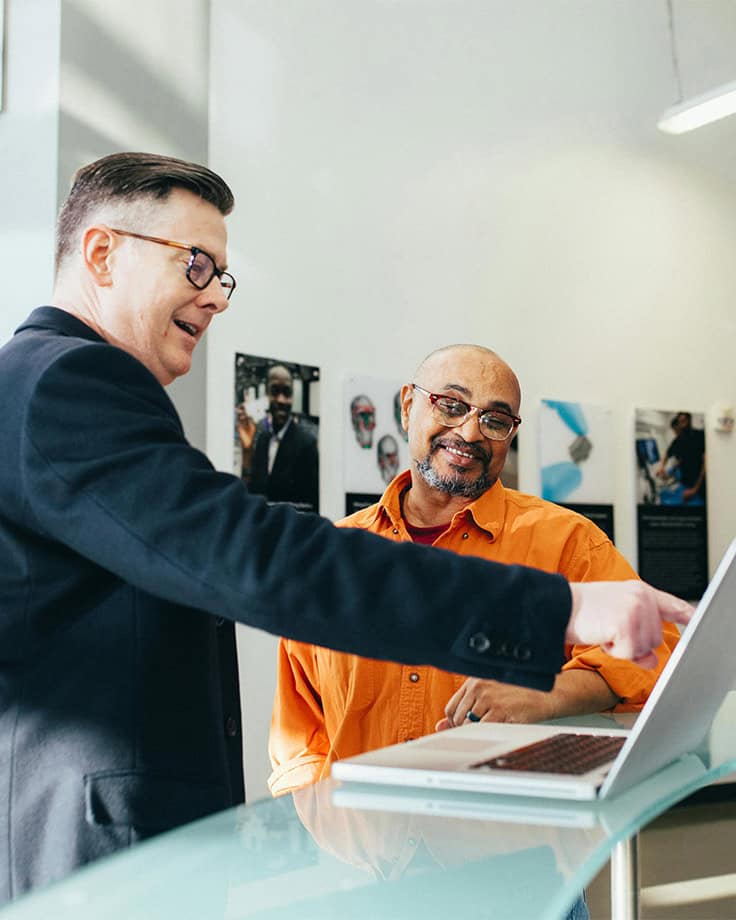 Two men collaborating over a laptop on a desk
