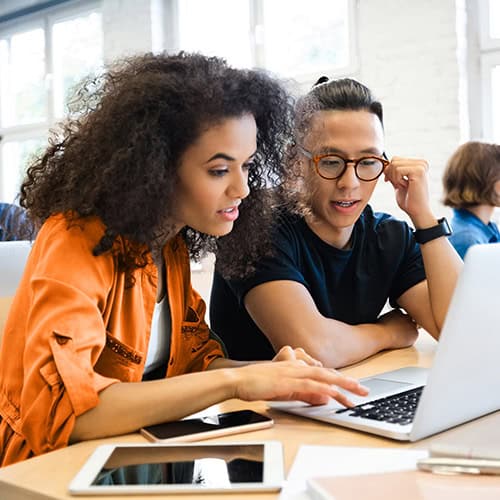 Two colleagues collaborating at a desk with a laptop