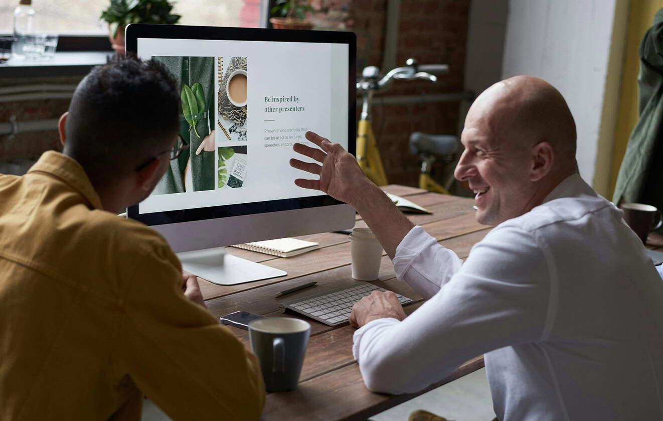 Two men sitting at desk collaborating in front of a computer