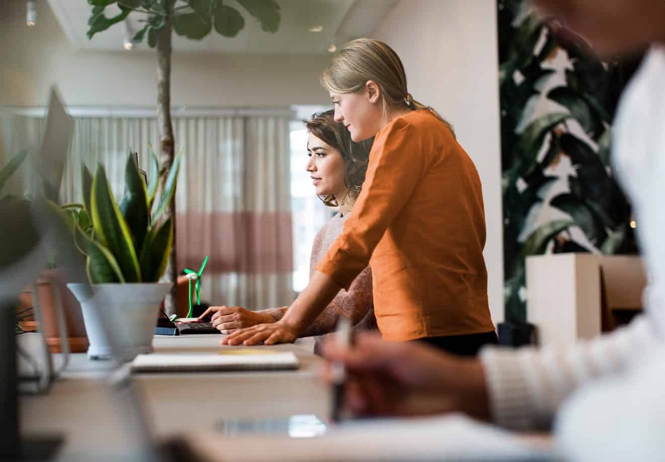 Two women collaborating at desk in front of desktop computer