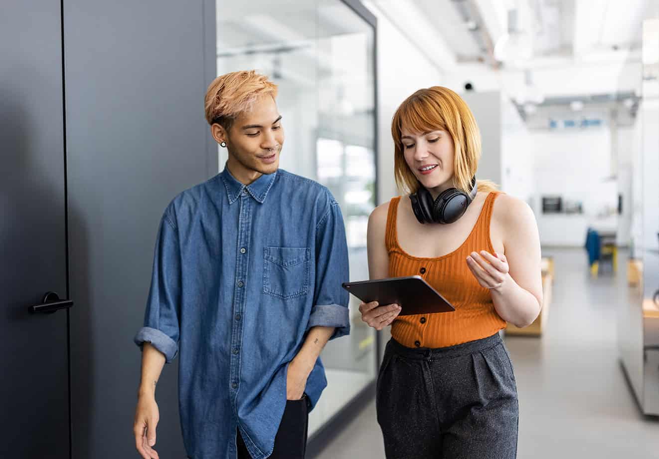 Two students walking down a hall talking over a tablet
