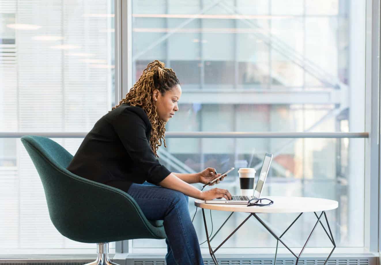 Woman sitting at a table and working on her laptop in front of a large window