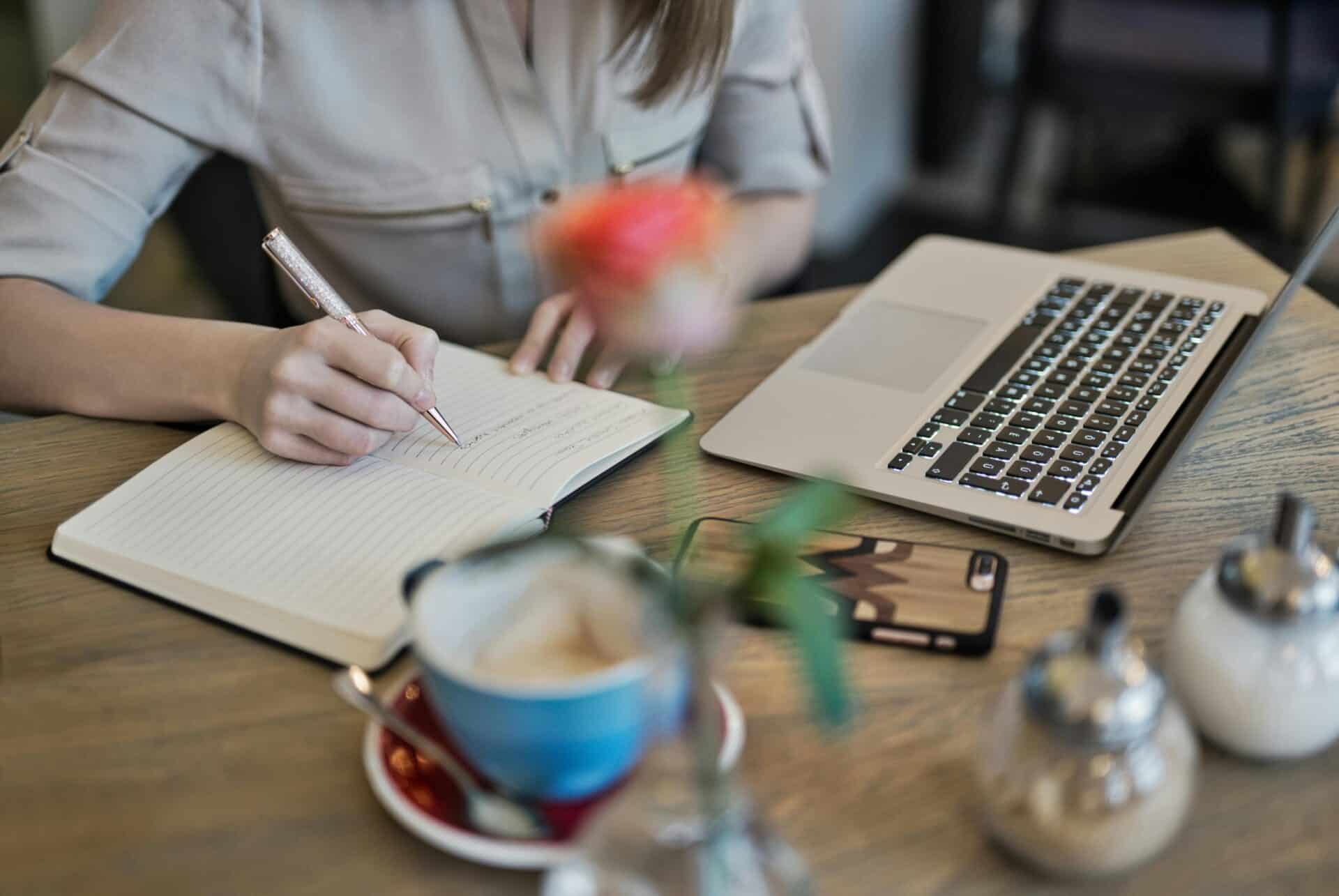 Person taking notes while reading off laptop