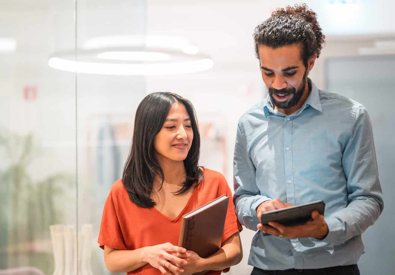 two people walking down a hallway talking while looking at a tablet