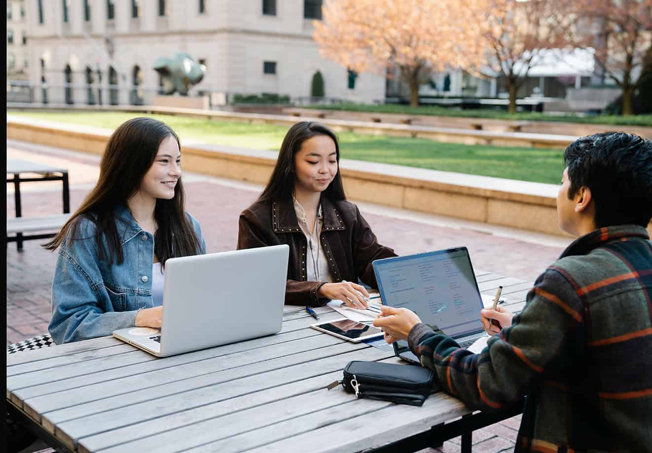 Three students sitting outside school working on laptops