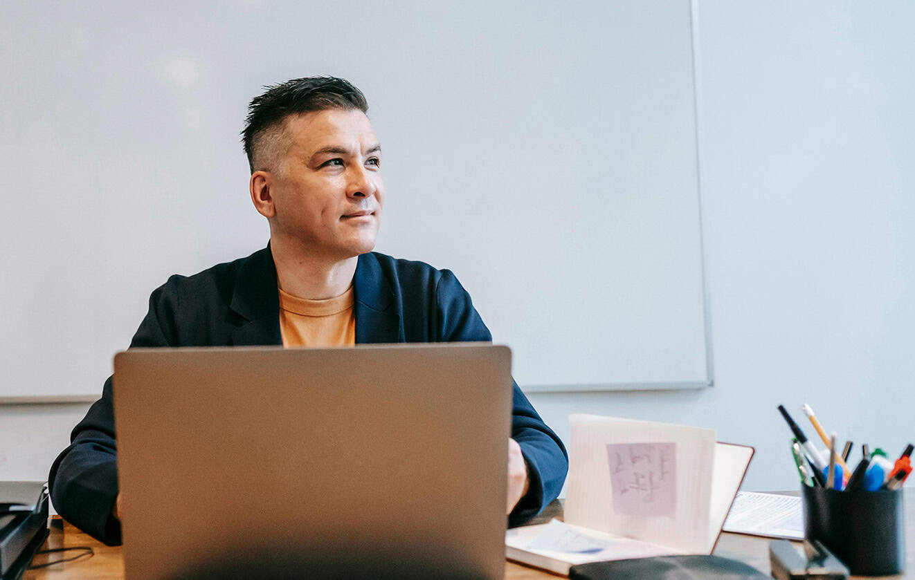 Man wearing blue blazer sitting at desk, working on laptop