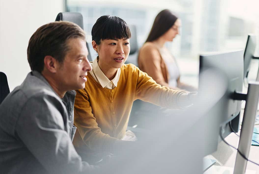 Two colleagues working together in front of computer desktop in open, modern office