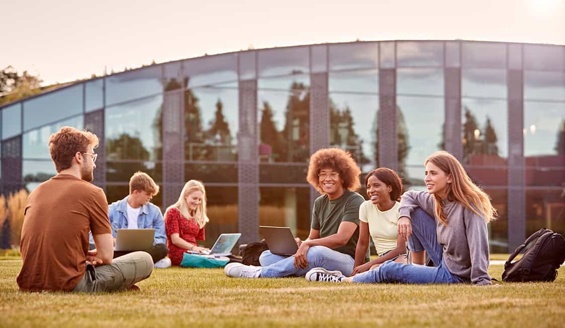 A group of students sitting on lawn outside of school