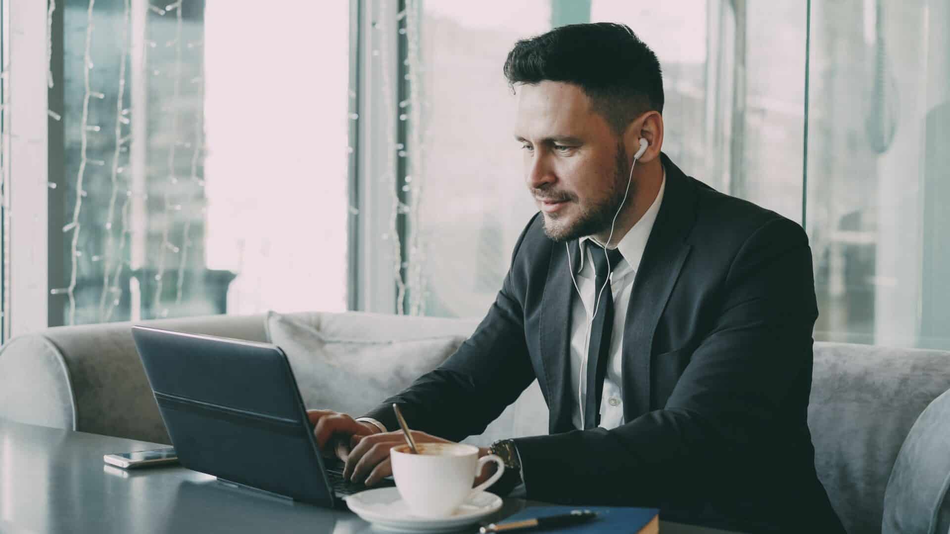 Business professional using a laptop with earbuds at a café table.