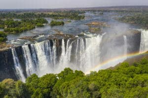 Aerial few of the world famous Victoria Falls with a large rainbow over the falls. This is right at the border between Zambia and Zimbabwe in Southern Africa. The mighty Victoria Falls at Zambezi river are one of the most visited touristic places in Africa.