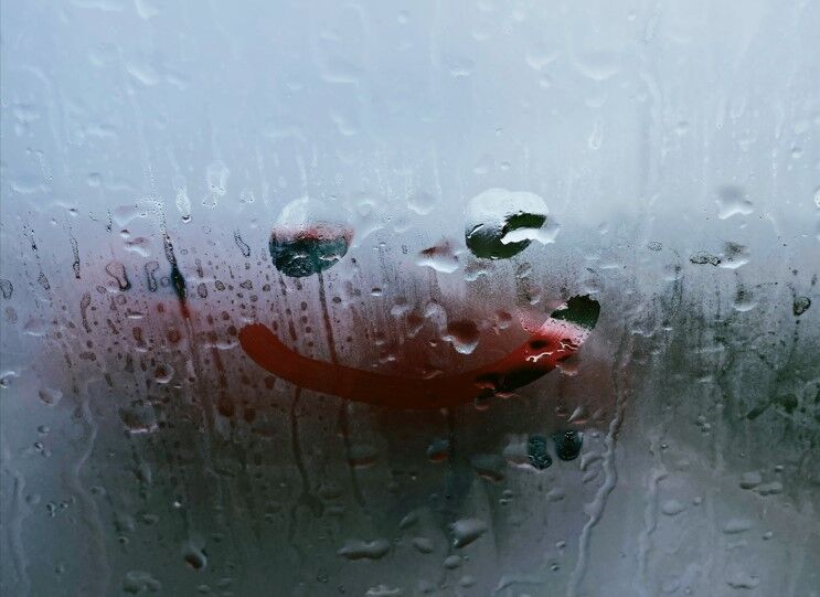 quelqu'un qui dessine un smiley sur une vitre avec de la buée