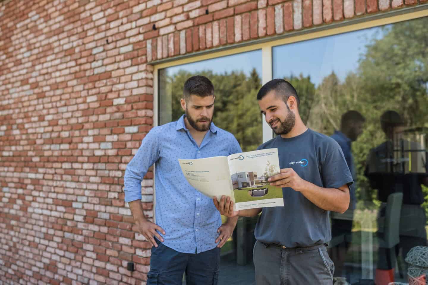 Conseiller eloy présentant à un client une brochure sur la microstation oxyfix®, ouverte sur la page des aides et subventions disponibles en France pour l’assainissement individuel.