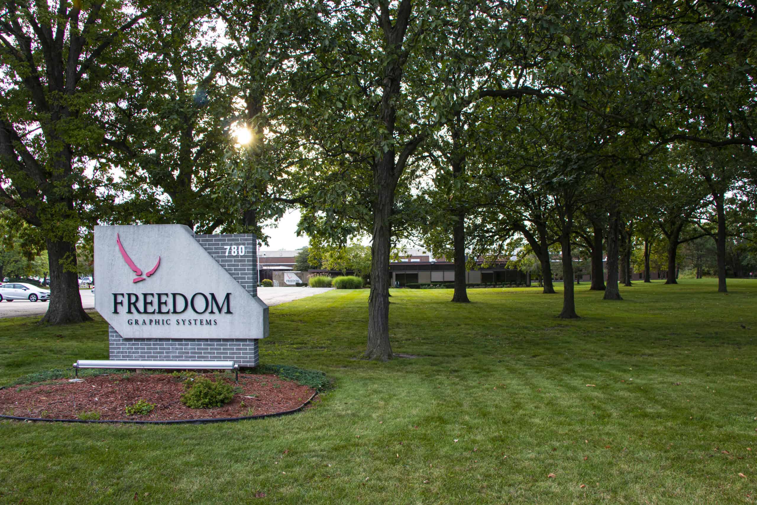 Outside at the Aurora Campus featuring pedestal signage, grass and trees.