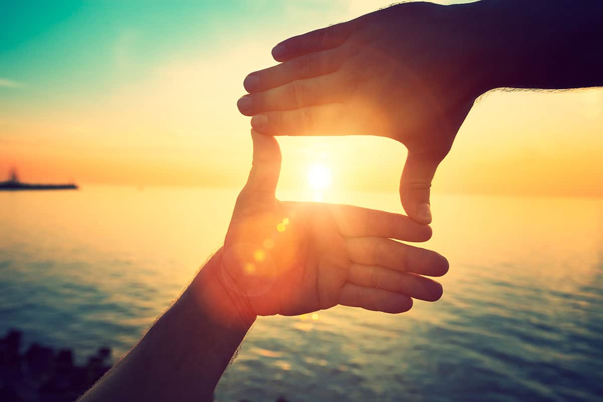 Silhouette of a pair of hands making a square shape, with the sunset in the background.