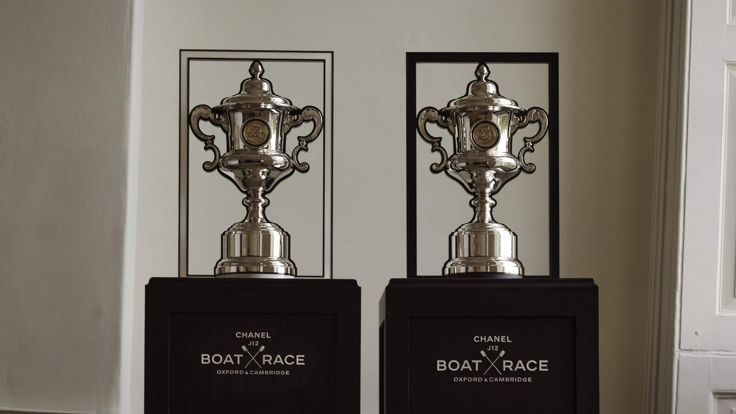 The CHANEL J12 Boat Race trophies in polished silver, the Women's trophy in a white frame and the Men's trophy in a black frame, on black plinths