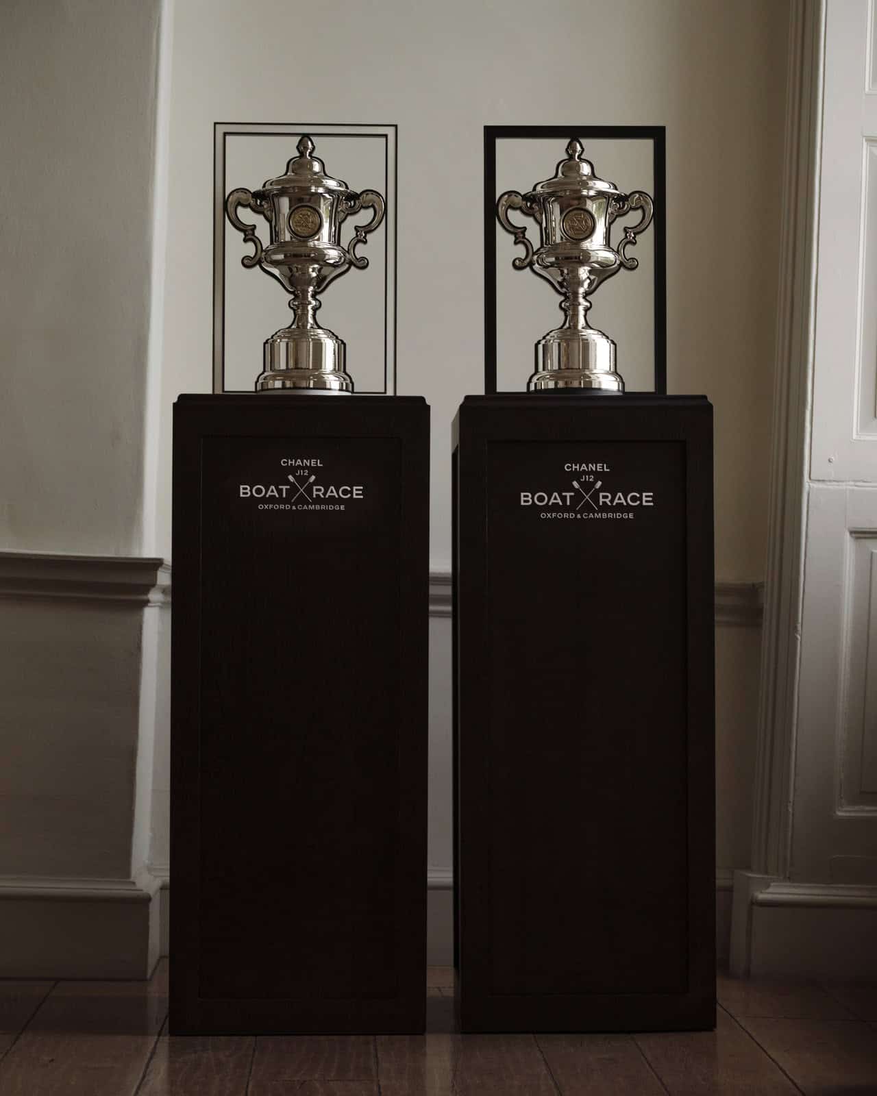 Two polished silver CHANEL J12 Boat Race trophies in white and black rectangular frames on black plinths marked CHANEL J12 Boat Race Oxford & Cambridge