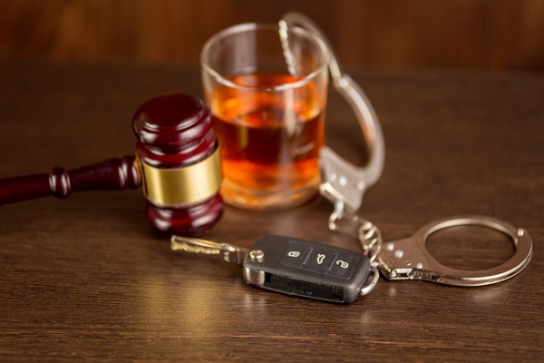 A set of car keys rests on a brown wooden table next to a glass, a pair ...