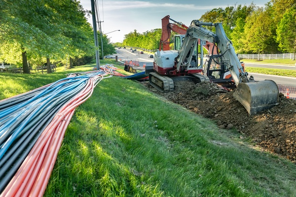 An excavator sits alongside the highway as it digs up the grass and ...