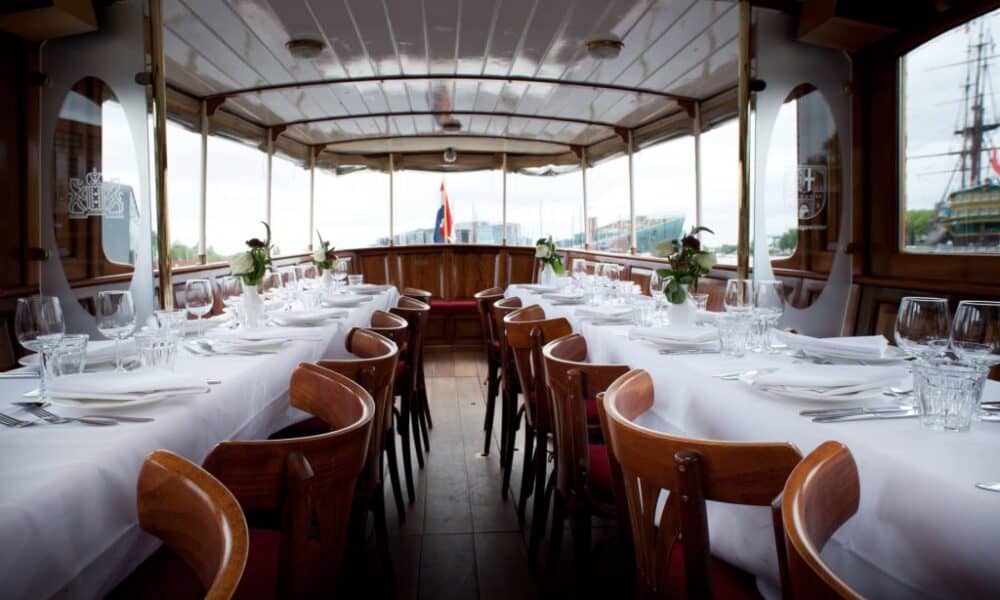 Elegant dining area on a boat with white tablecloths and wooden chairs. A perfect setting for a city trip to Amsterdam.