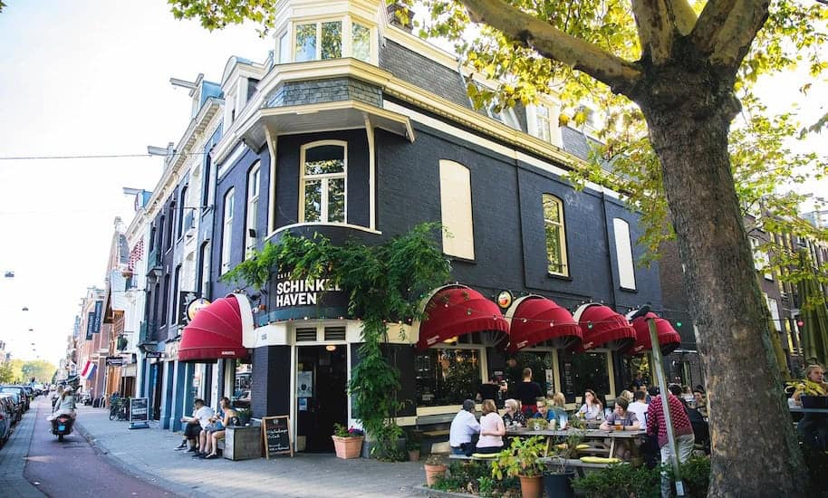 Invitados sentados frente al Café Schinkelhafen negro con toldos rojos
