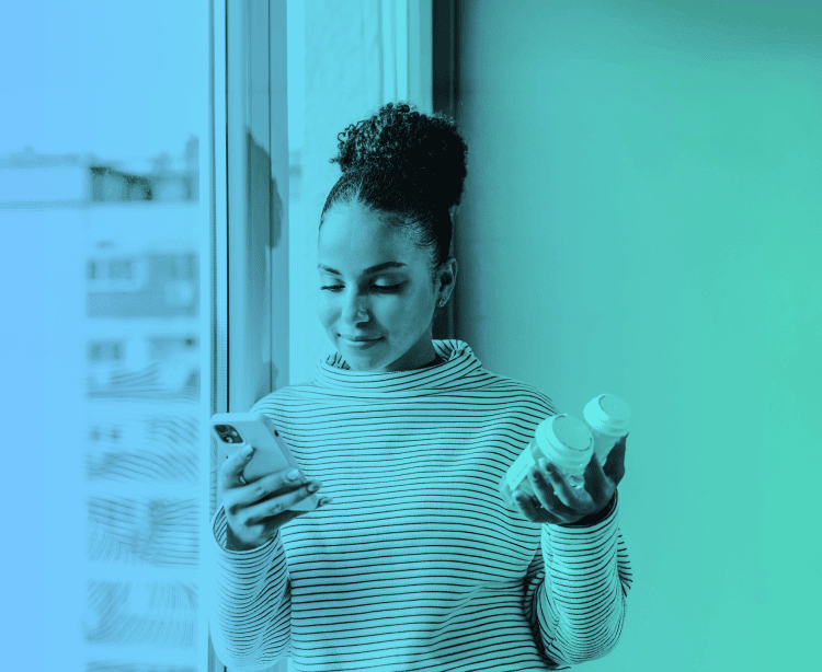 A woman holding a couple of medication bottles in one hand and her smartphone in the other